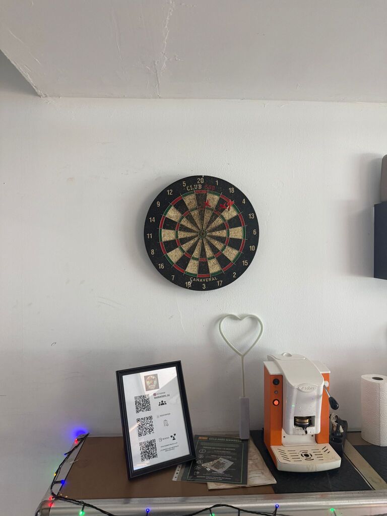 A dartboard on the wall above a shelf with a coffee machine.