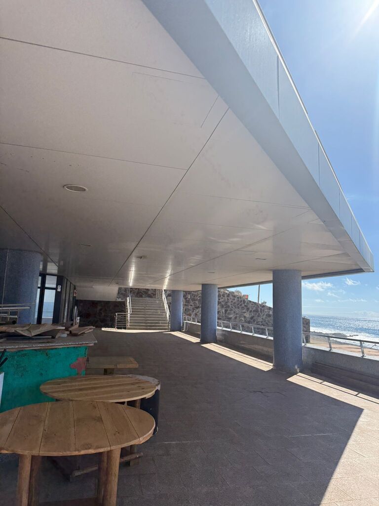 Round wooden tables on the covered terrace, under the concrete canopy.